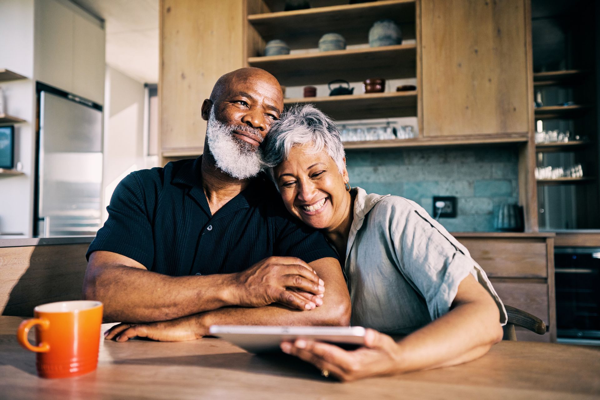 An elderly couple is sitting at a table looking at a tablet.