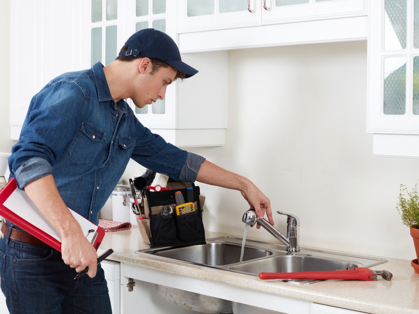 A plumber is fixing a faucet in a kitchen.