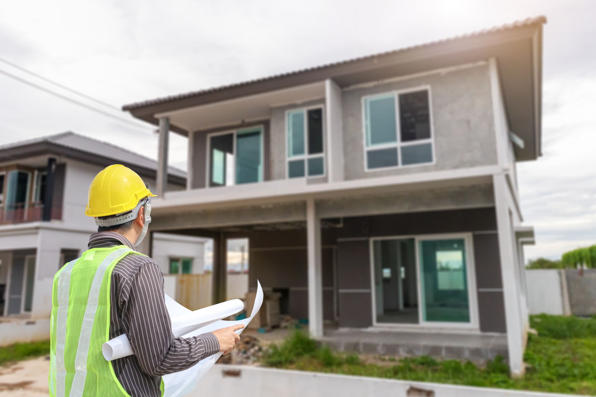 A construction worker is standing in front of a house under construction.