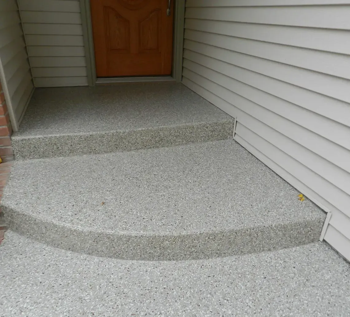 Two steps leading to a front door, finished with a gray speckled epoxy coating against brick and siding walls.