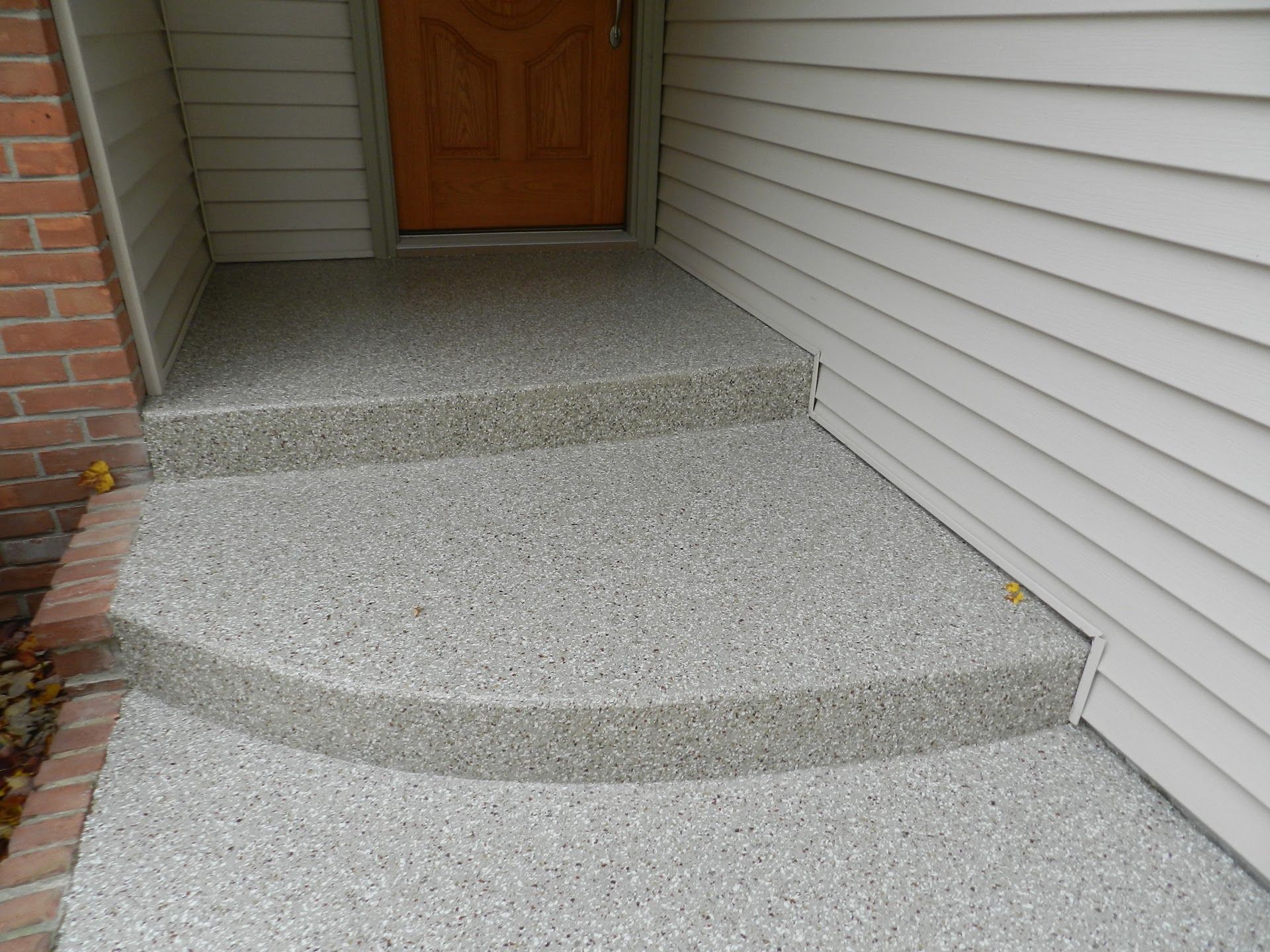 Two steps leading to a front door, finished with a gray speckled epoxy coating against brick and siding walls.