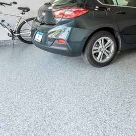 A dark gray car parked in a garage with a light gray speckled epoxy floor and a bicycle leaning against the wall.
