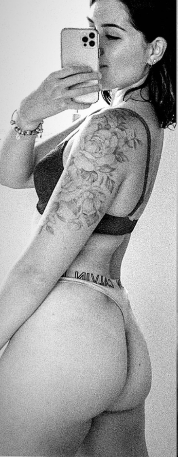 Woman in lingerie takes a mirror selfie, showing off a tattoo on her arm.