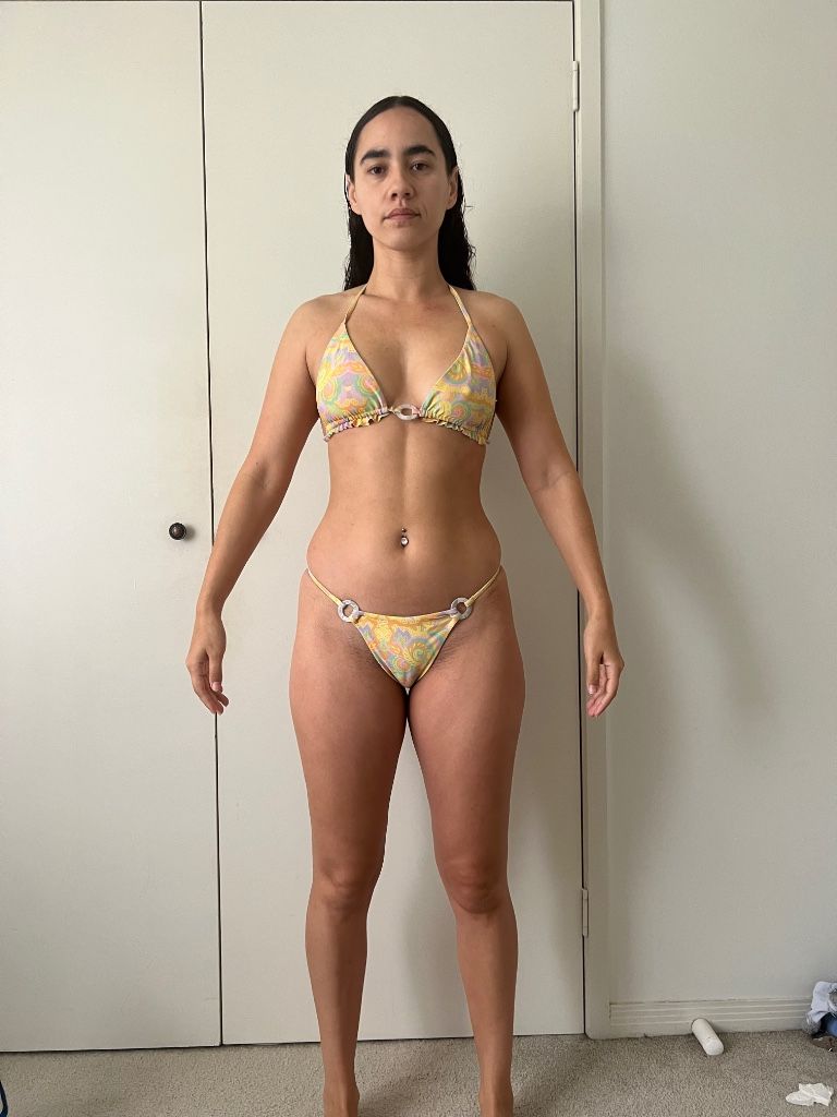 Woman in yellow bikini stands in front of a white door, arms outstretched.