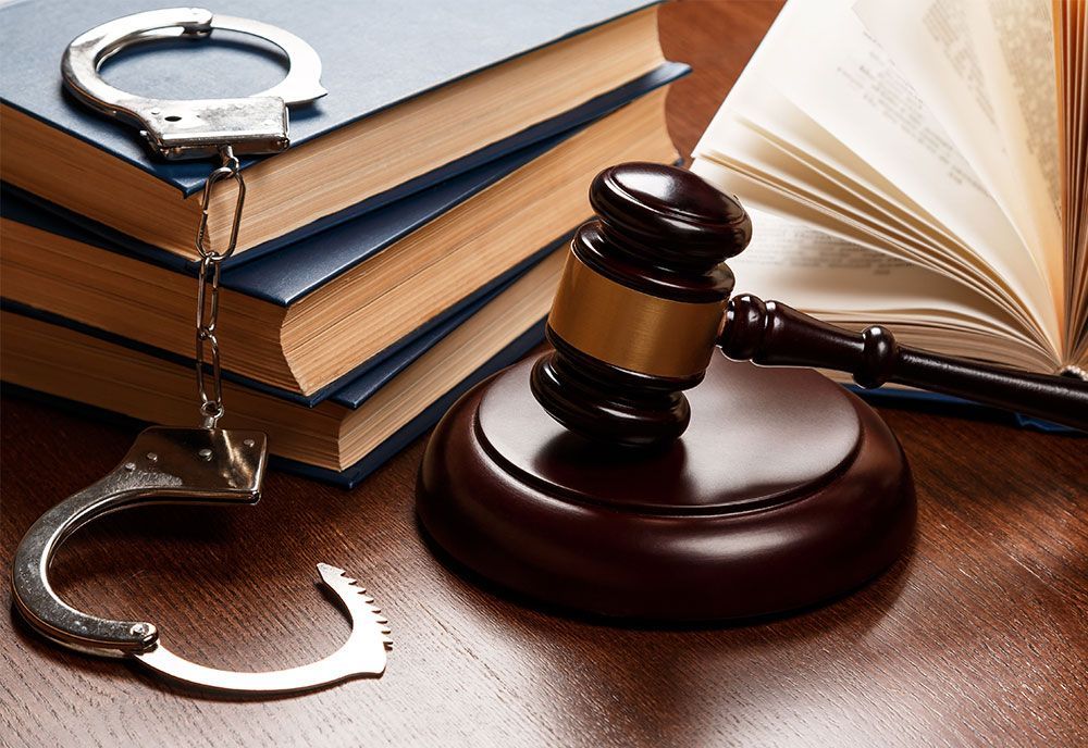 A wooden gavel on a base, a stack of books, and silver handcuffs on a polished brown wooden table.