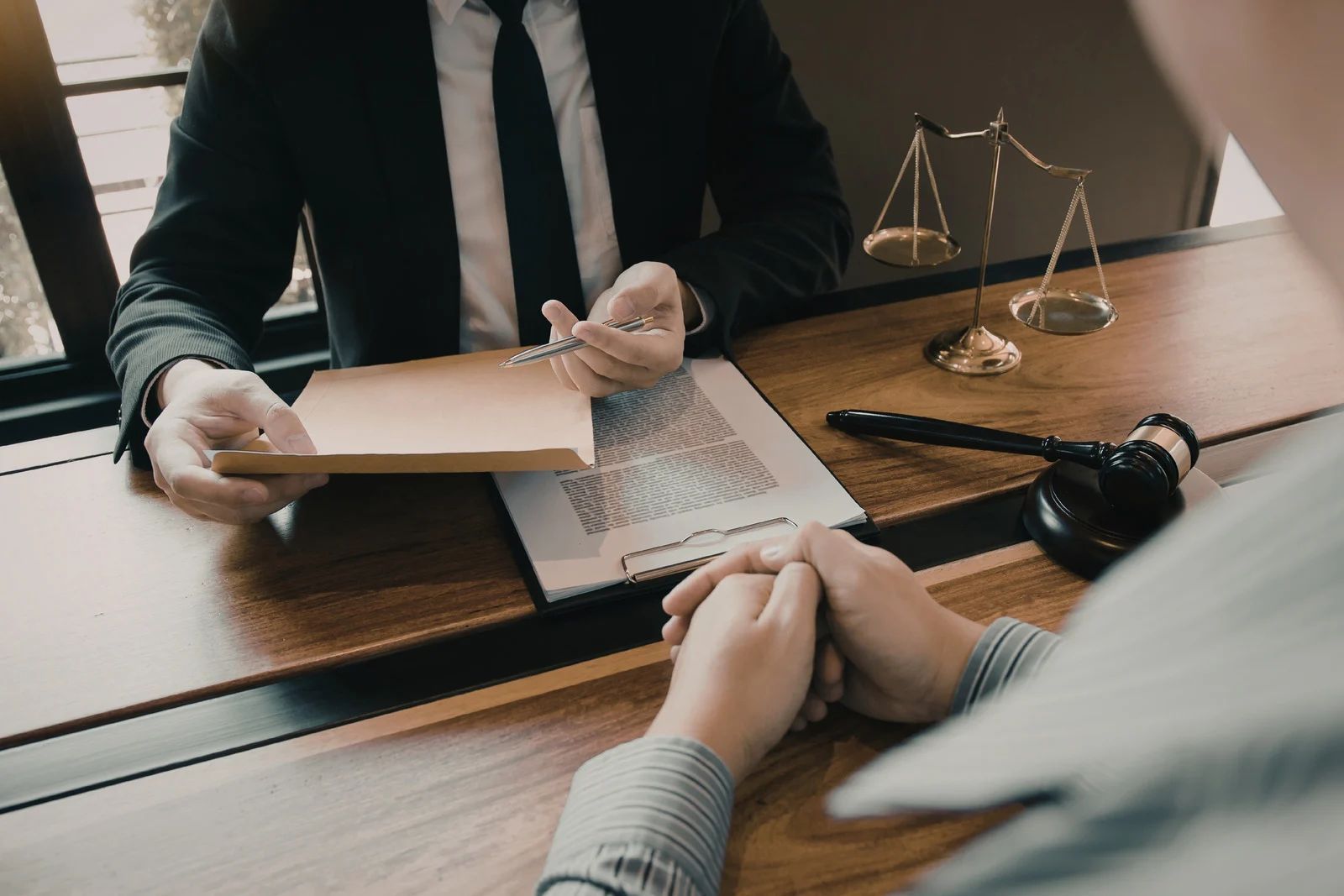 Two people review documents across a law office desk with a scales of justice ornament.