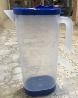 Jarra de plástico transparente con tapa, base y asa de color azul.