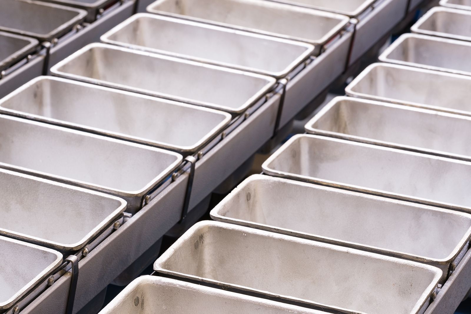 Filas de moldes de pan metálicos rectangulares y vacíos sobre una rejilla, probablemente en una panadería.