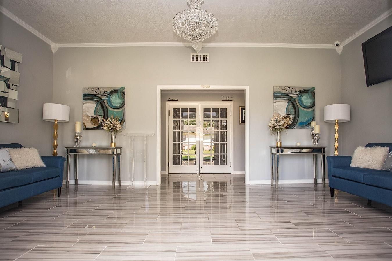 Elegant foyer with blue sofas, mirrored tables, artwork, and crystal chandelier.