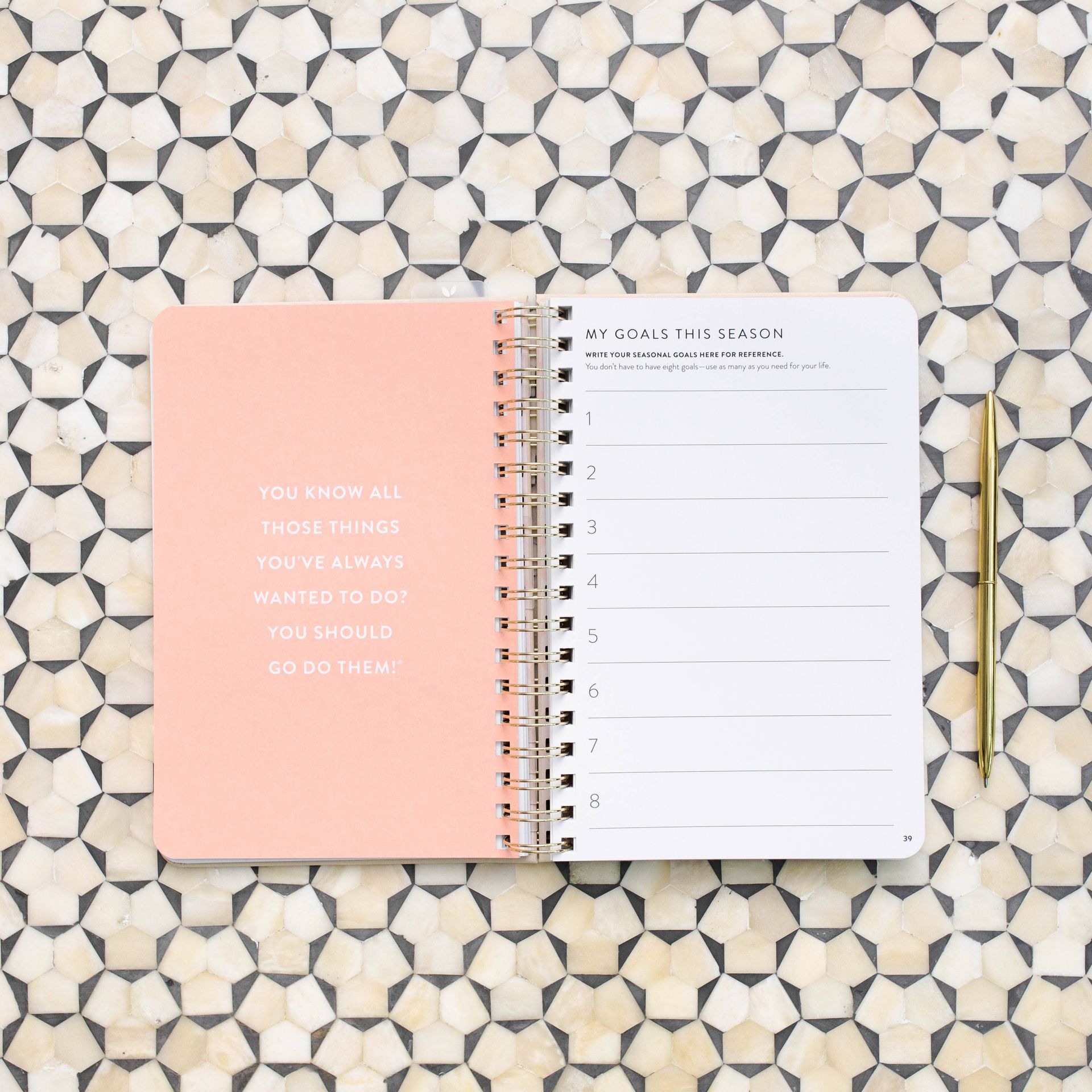 A spiral notebook is sitting on a table with a pen.