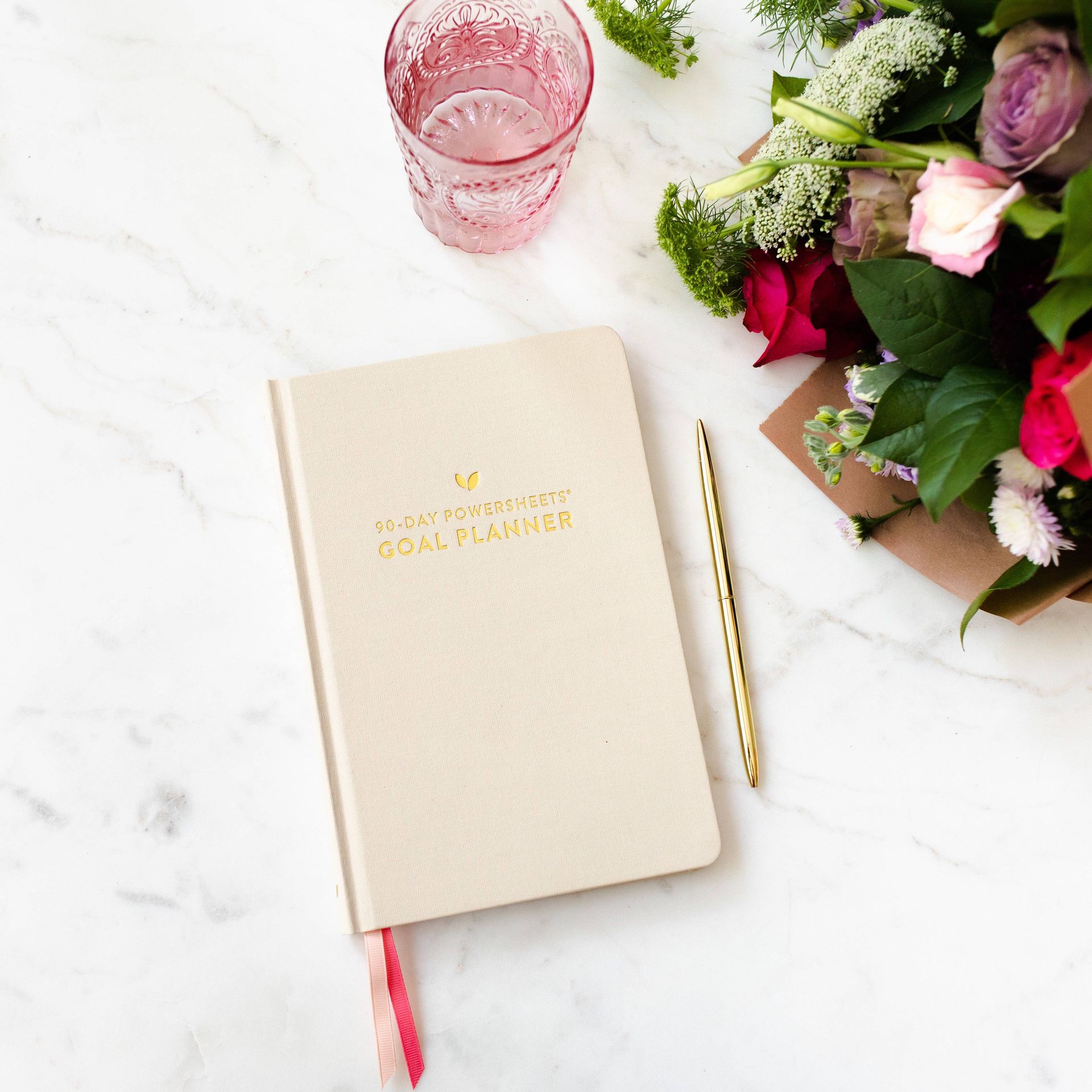 A planner is sitting on a table next to a bouquet of flowers and a glass of water.