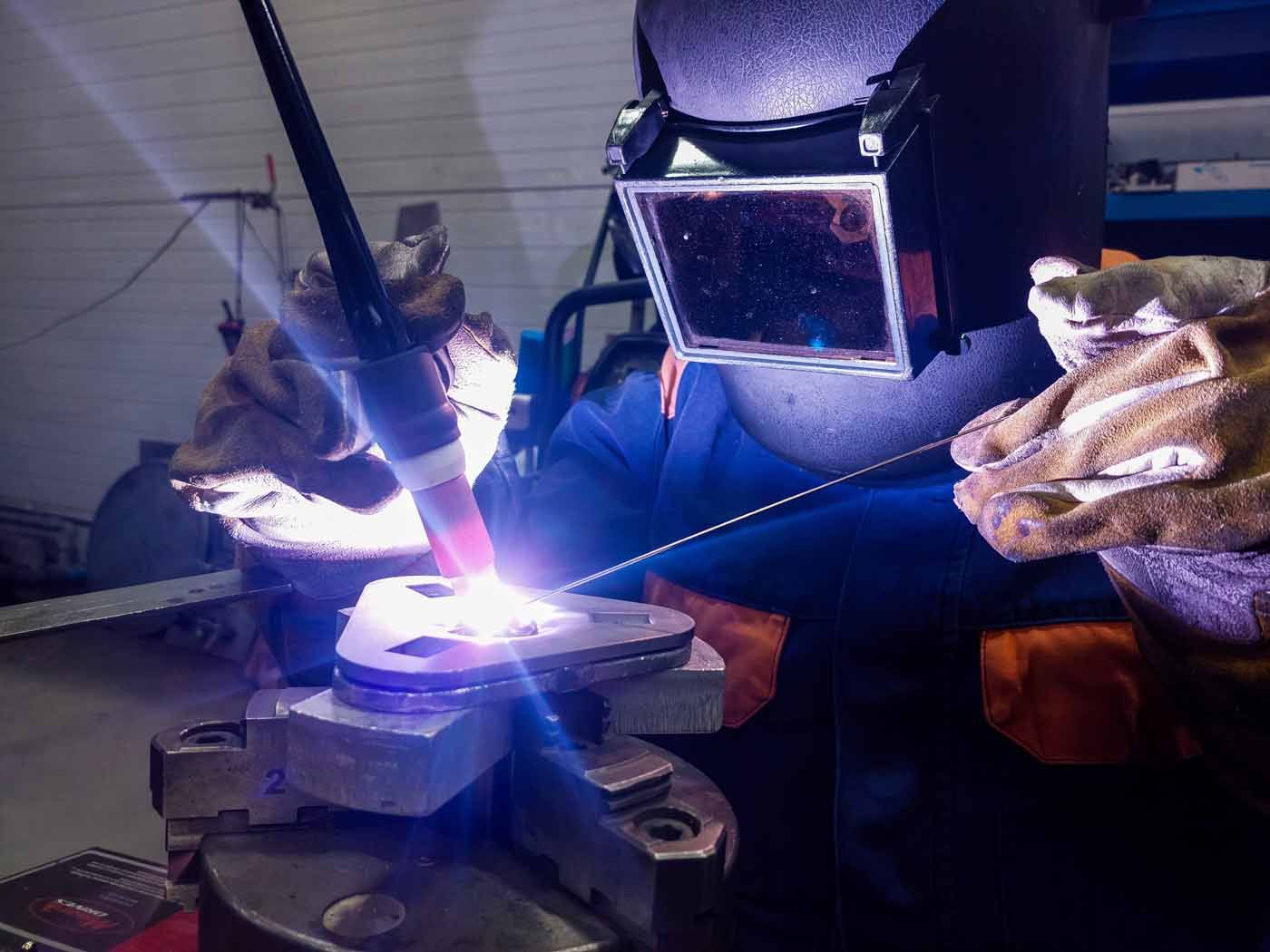 A man wearing a welding mask is welding a piece of metal.