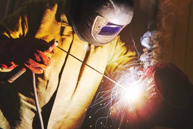 A man wearing a welding mask is welding a piece of metal.