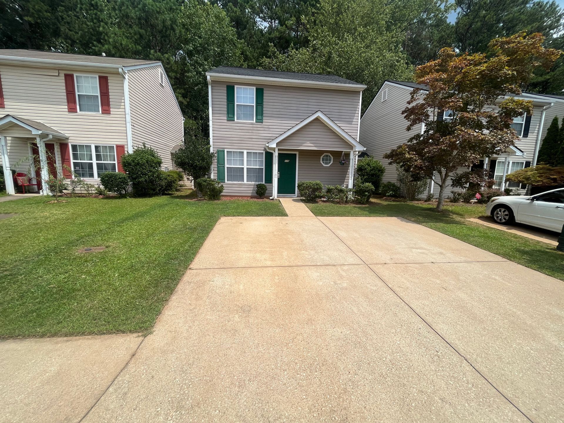 Tan two-story house with a green door and shutters, situated between two other houses, with a concrete driveway.