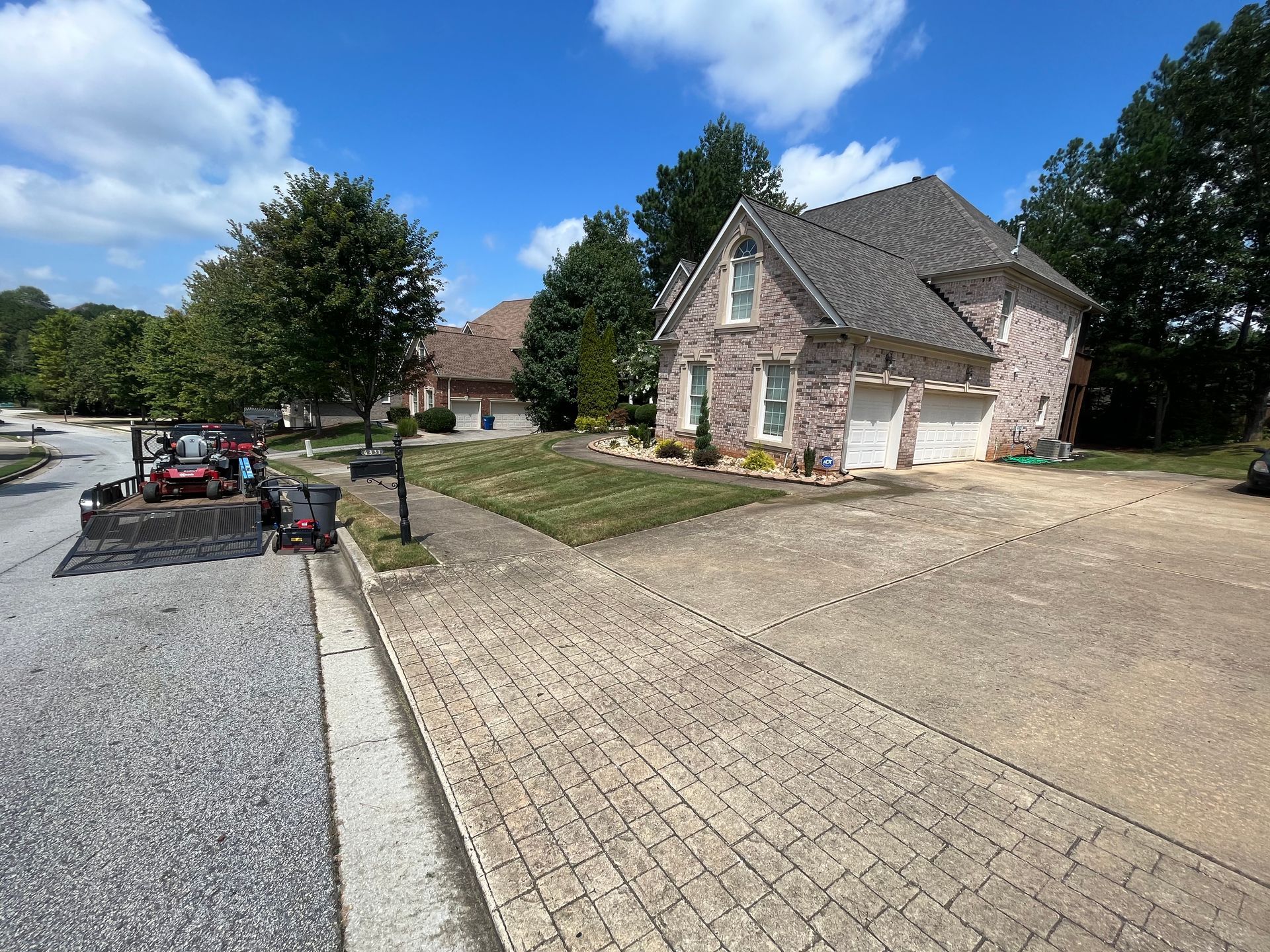 Brick home with manicured lawn and brick paver driveway under a blue sky.