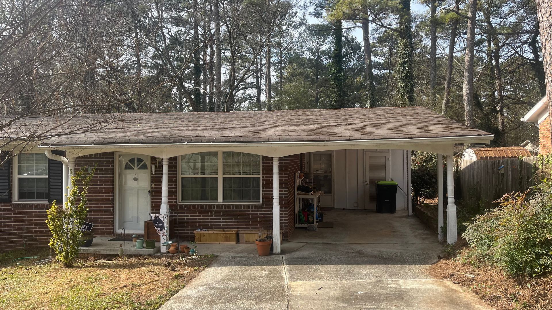 Low brick house with carport; driveway, grass, and trees.