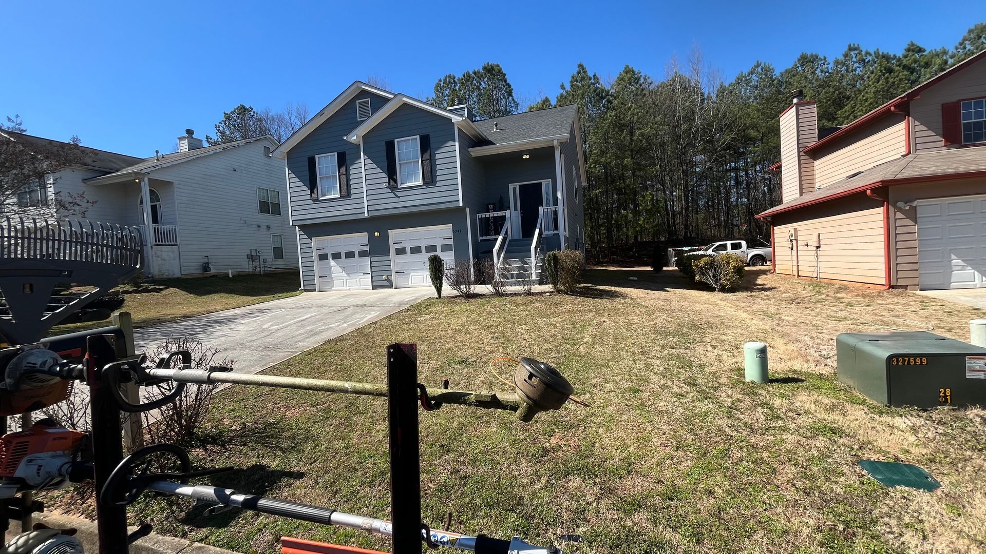 Blue house with white garage doors and a brown roof; a lawnmower is in the foreground.