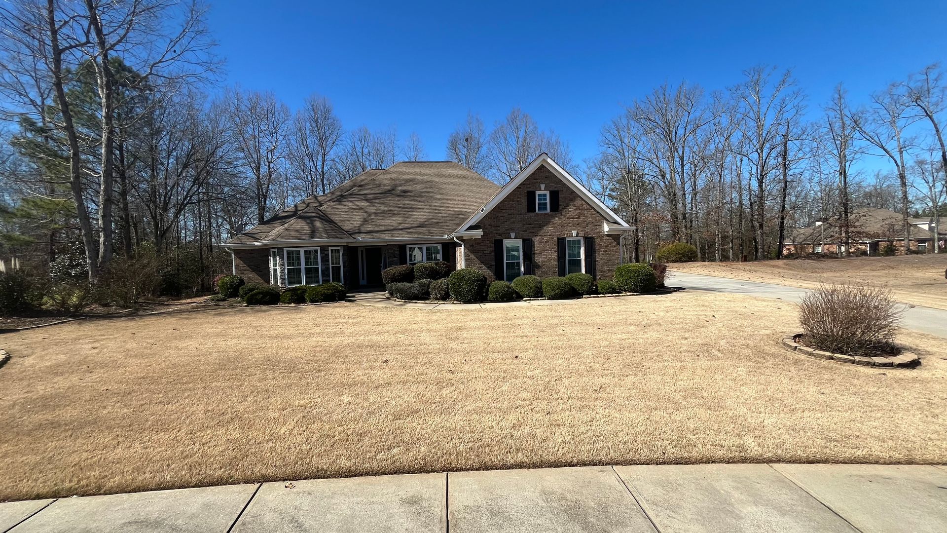 Brick house with brown roof and dry brown yard under a clear blue sky.
