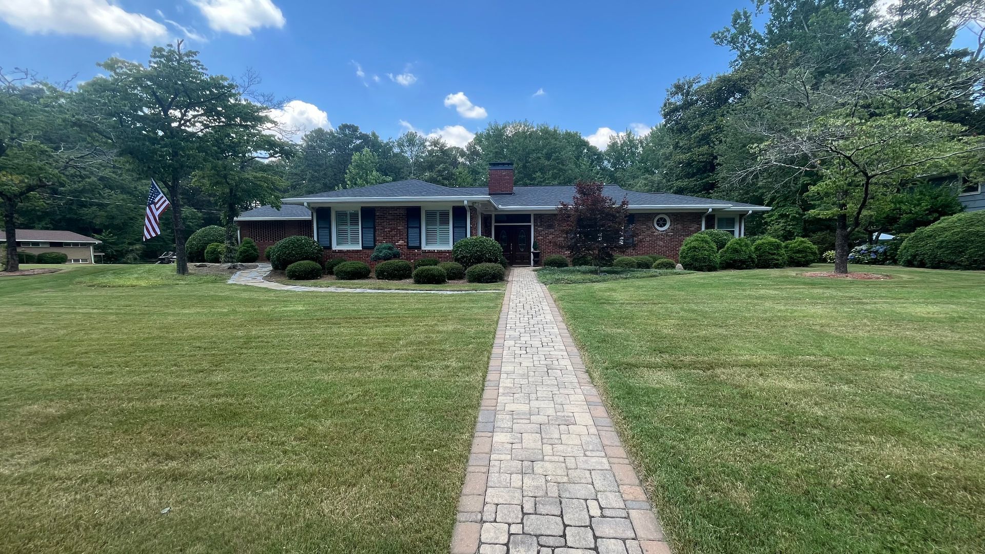 Brick ranch home with a brick pathway leading to the front door. Green lawn and trees surround the house on a sunny day.
