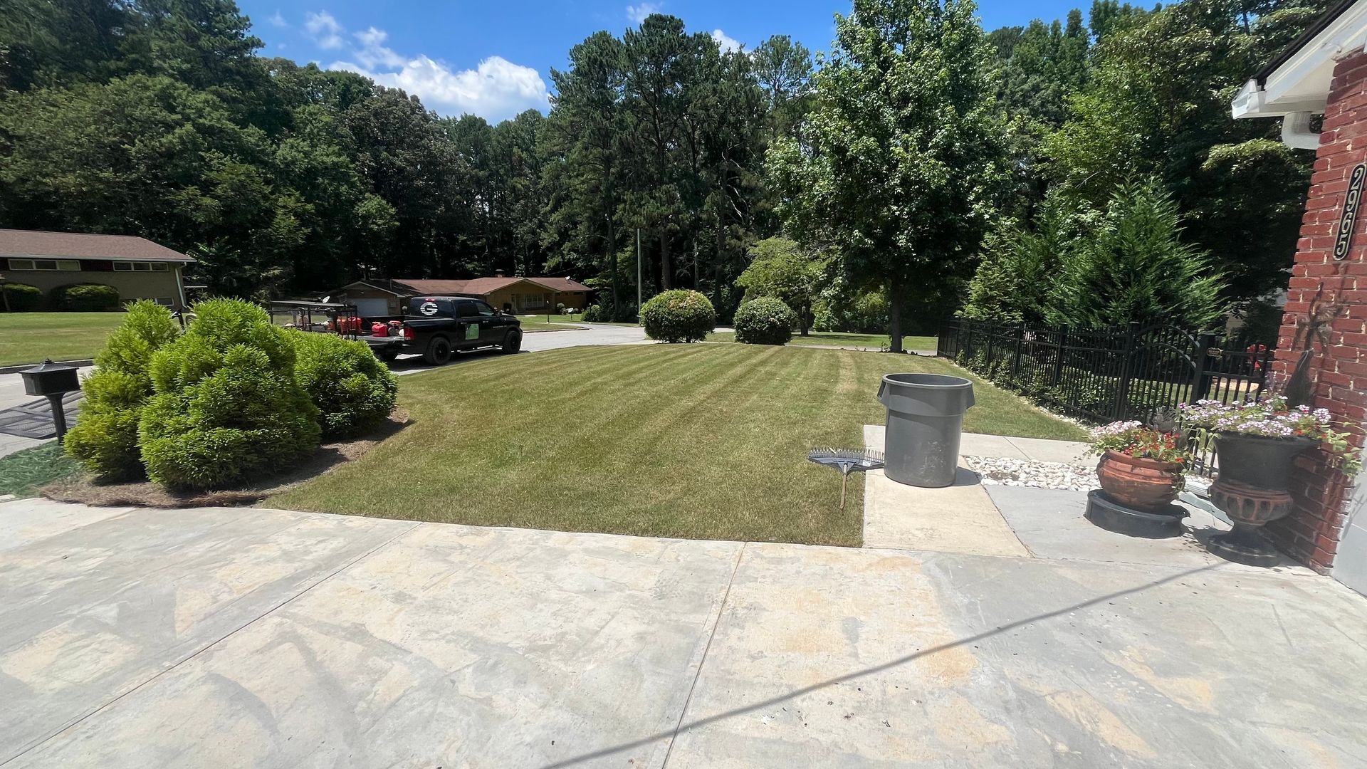 Lawn with freshly cut grass, a black car, and trees. A gray trash can and small bushes are present.
