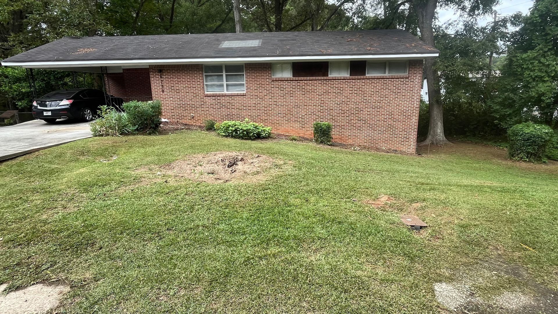 Brick house with carport. Green lawn, shrubs, car parked under carport.