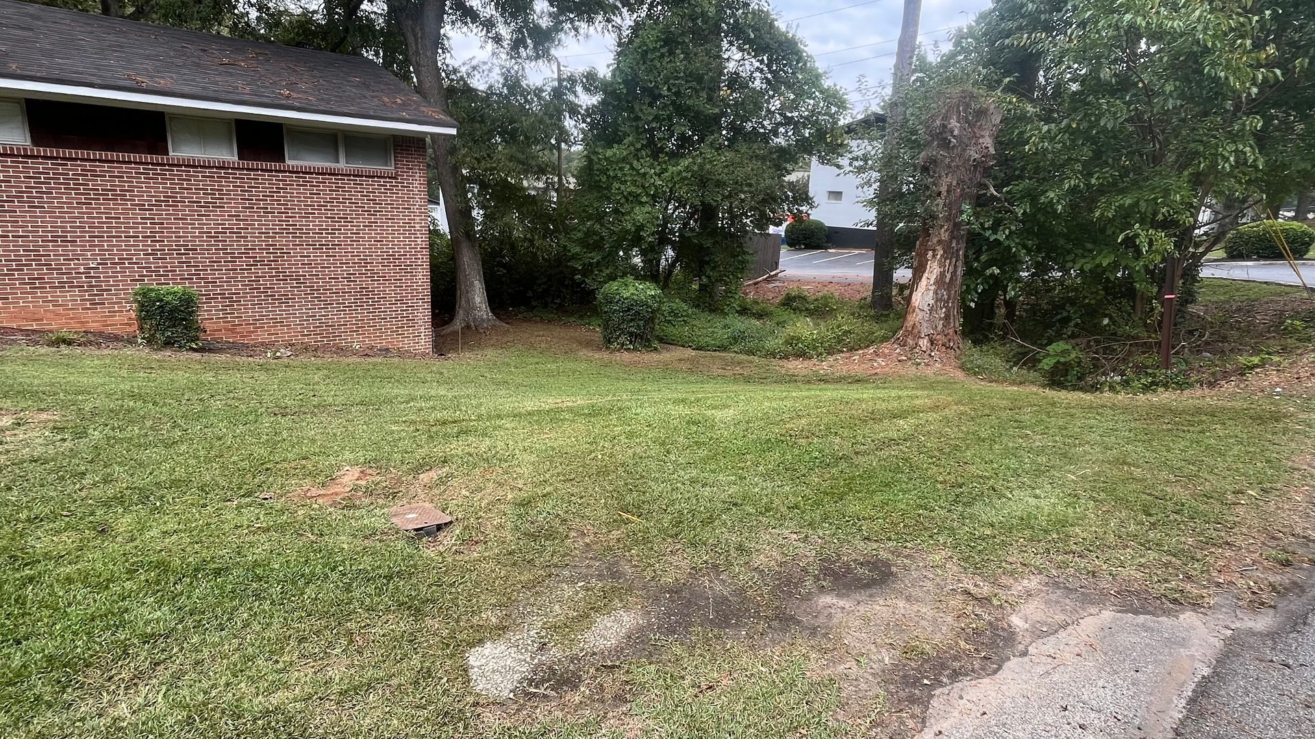 Brick building next to grassy lot with trees and a sidewalk.