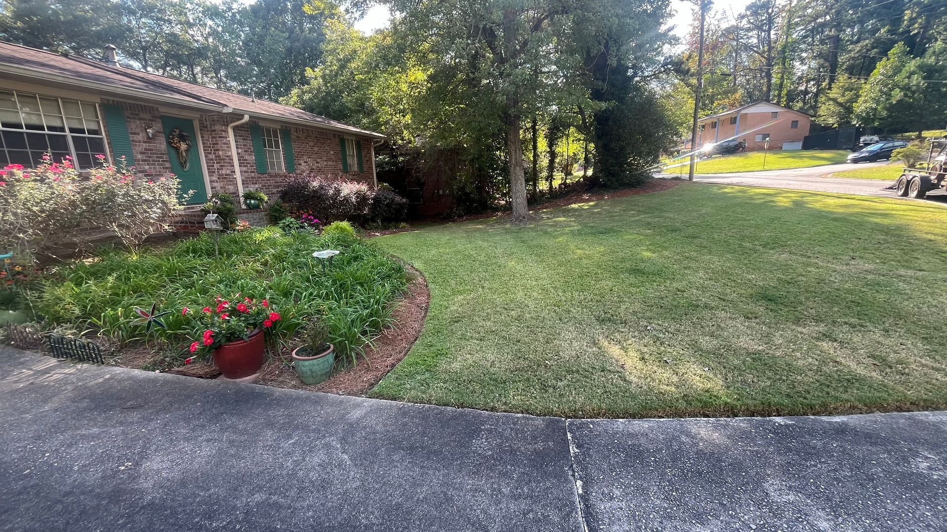 Brick house with green shutters, a well-manicured lawn, and lush flower beds. Sunny day.