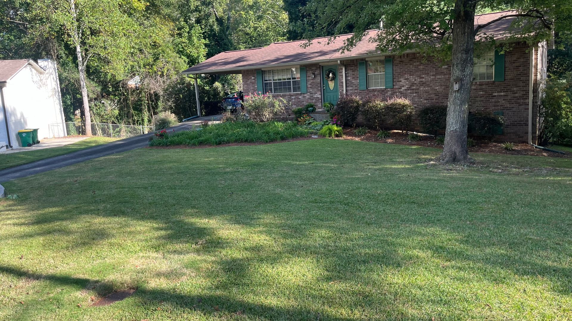 Brick ranch-style house with green trim, brown roof, and lush green lawn.