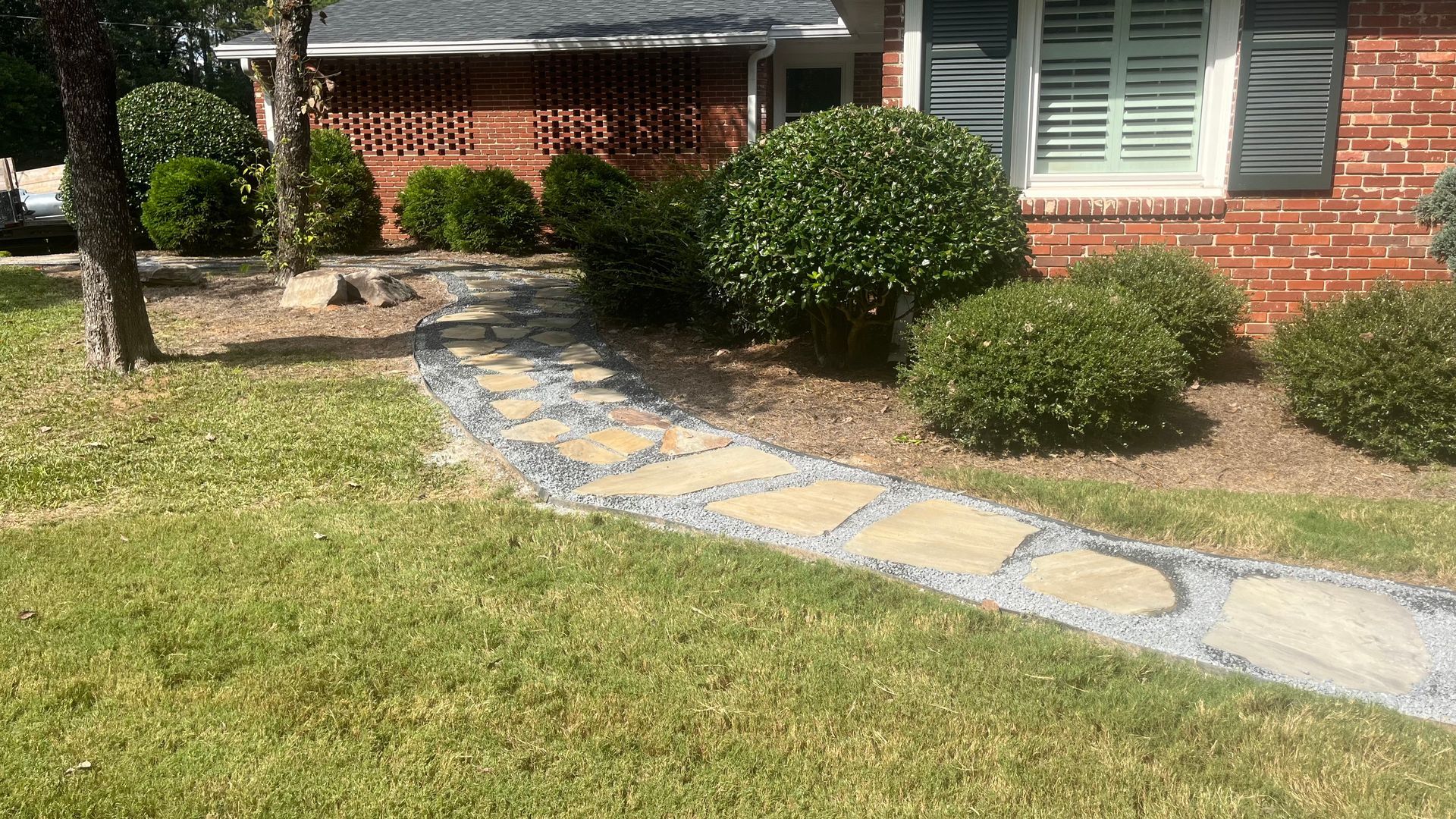Stone path leading to a brick house, flanked by green bushes and grass.