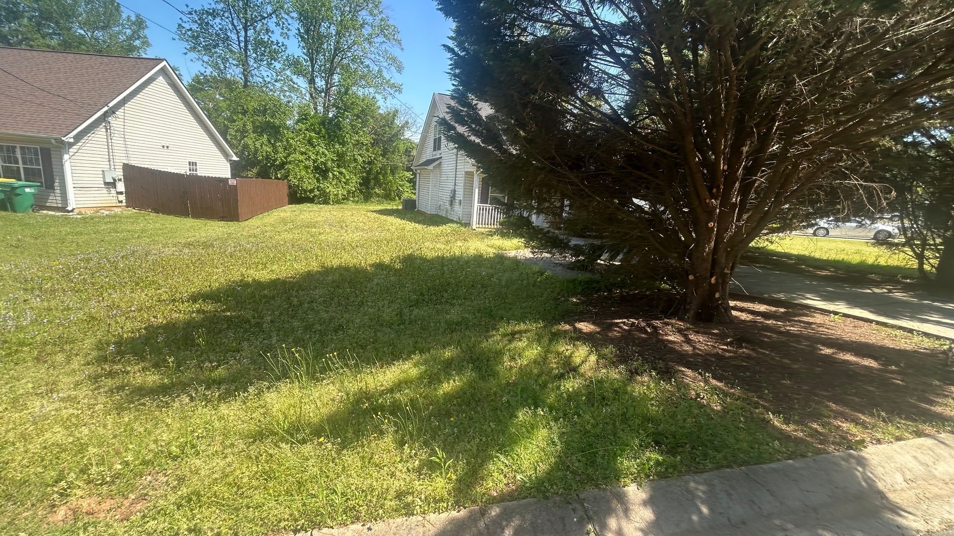 Grassy yard with a house and tree on a sunny day.