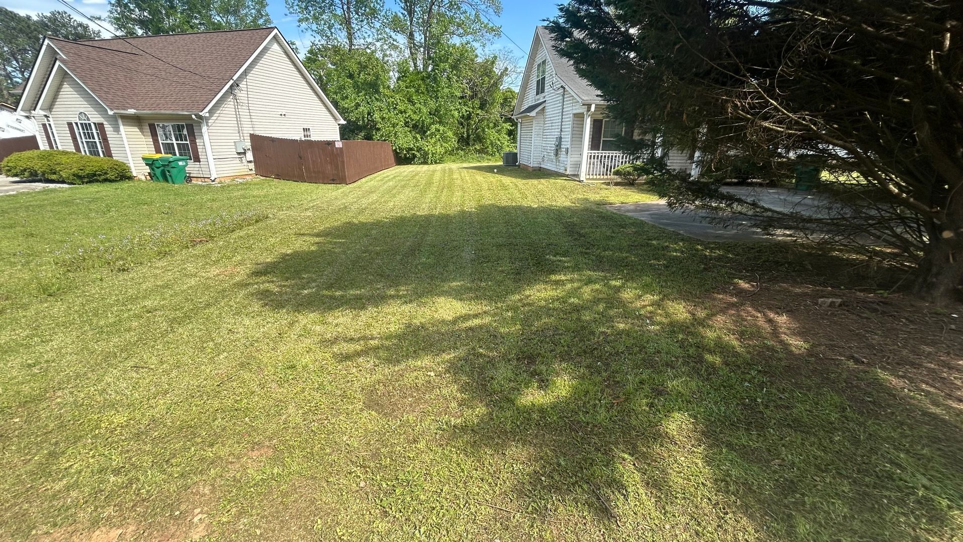 A grassy yard between two houses. Sunlight casts shadows on the freshly mowed lawn.