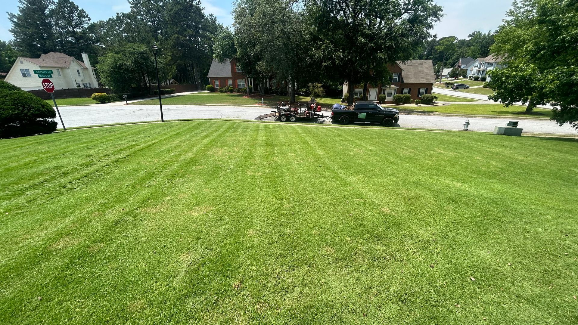 Lawn, freshly mowed, with a lawn care crew, truck, and trailer parked on a gravel driveway.