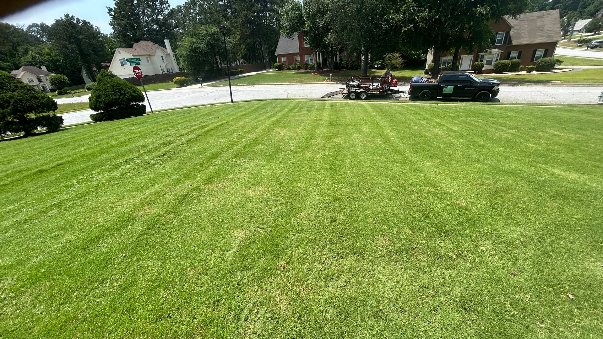 Green lawn freshly mowed, with houses and lawn equipment in the background on a sunny day.
