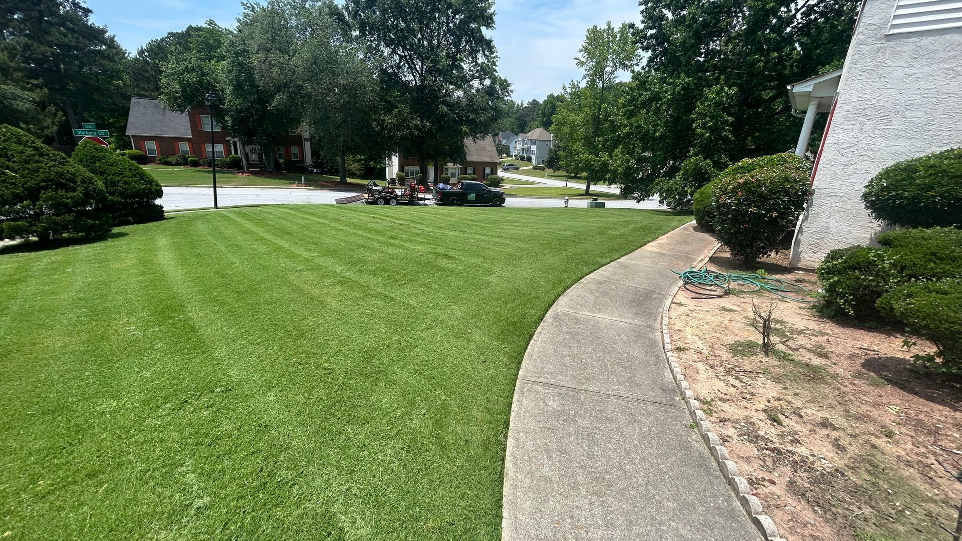 Green lawn with freshly cut stripes, sidewalk, and house on a sunny day.