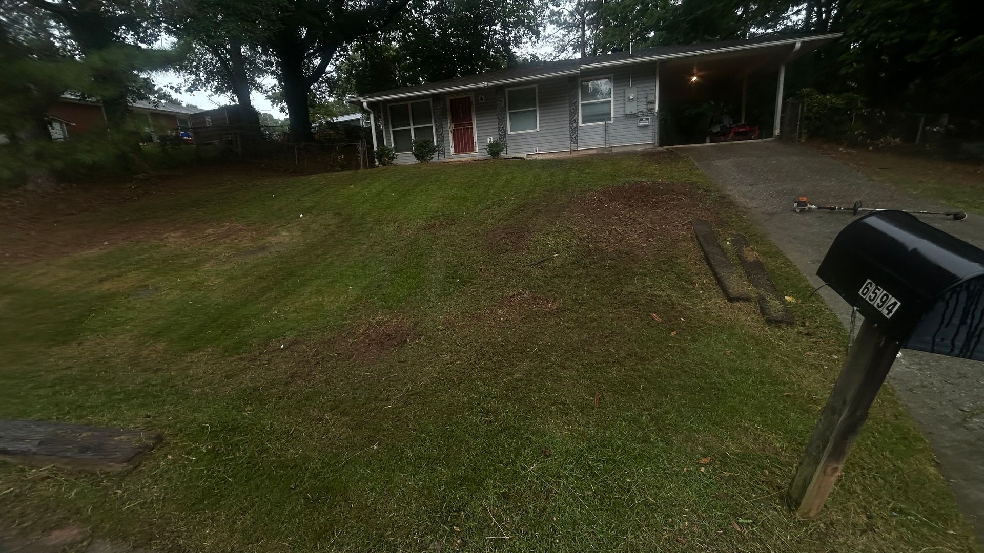 Gray house with a carport, mailbox, and grassy front yard.