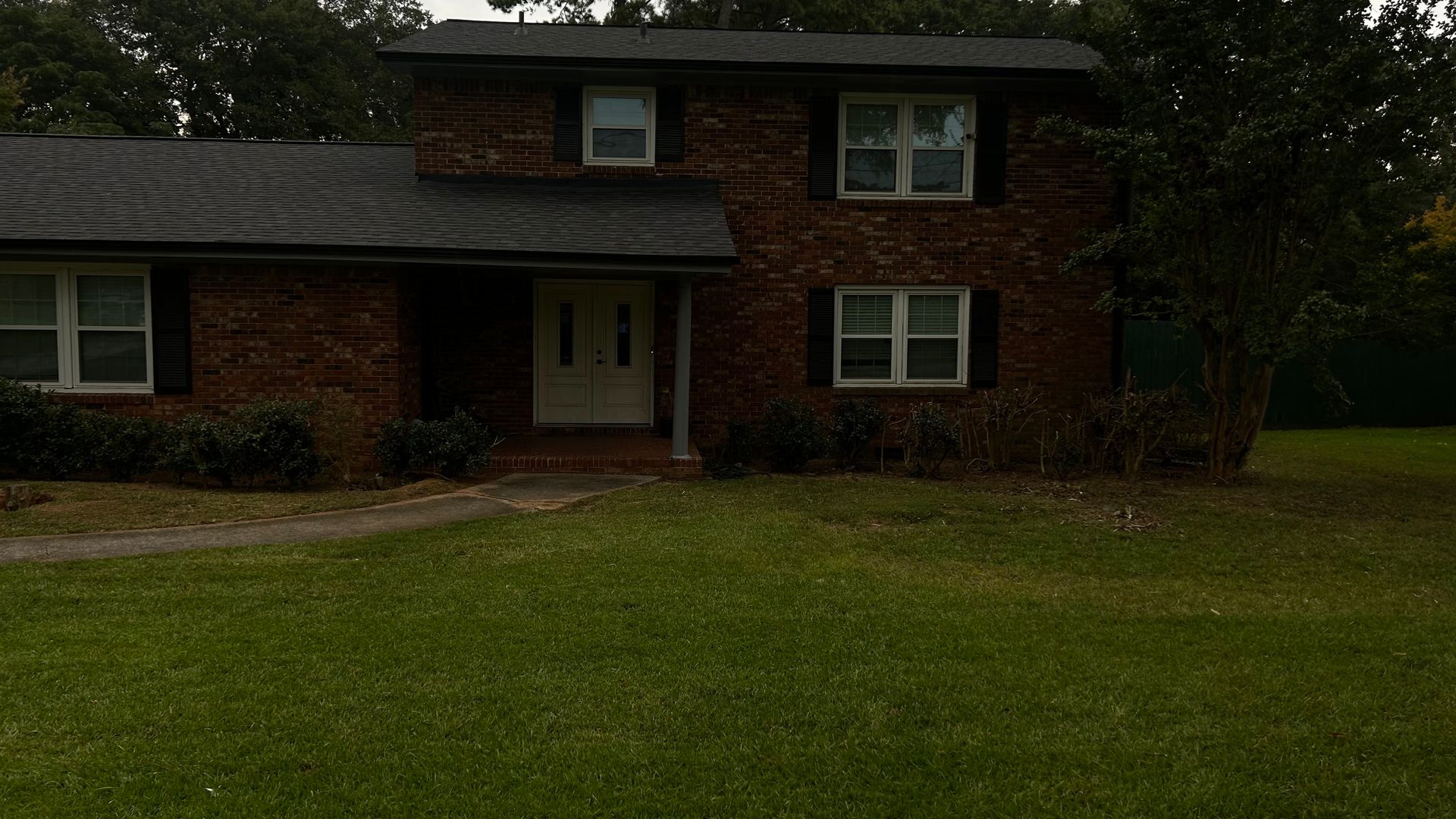 Two-story brick house with a dark roof and a white front door. Green lawn in the foreground.
