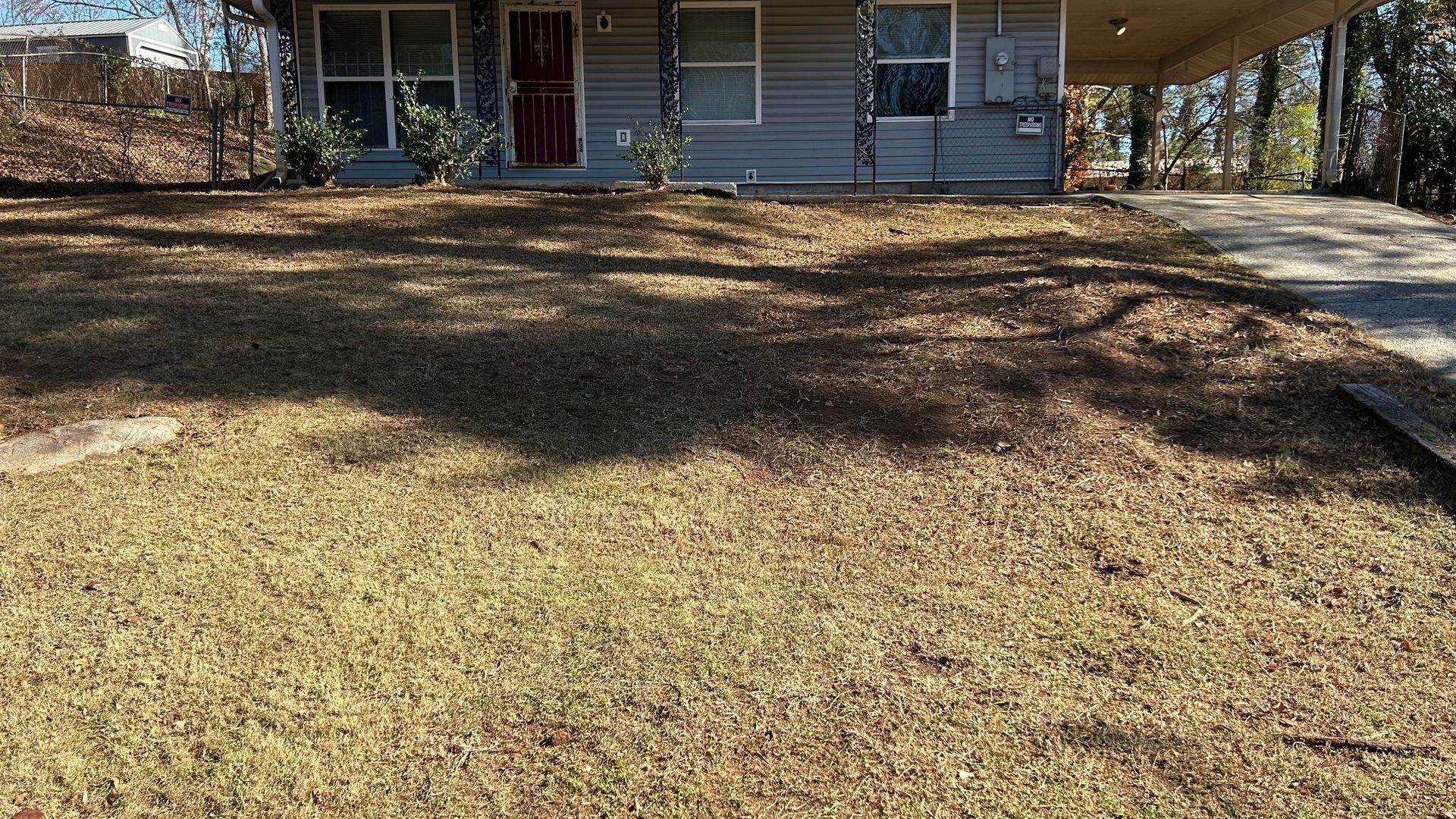 A single-story house with a brown yard and a covered carport. The house is painted gray.