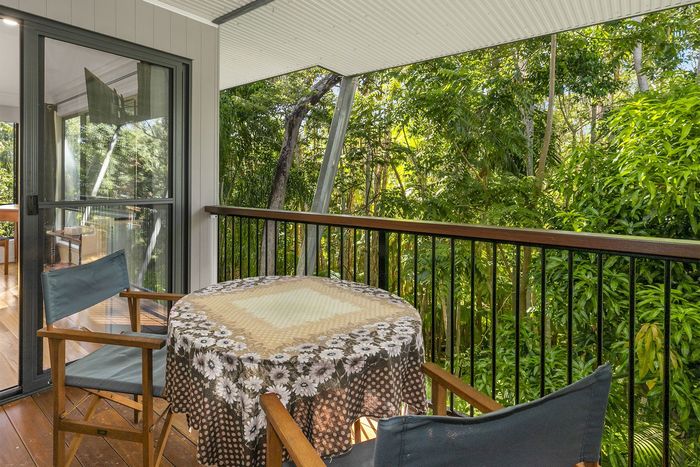 A balcony with a table and two chairs overlooking lush greenery. The table is covered with a patterned tablecloth.