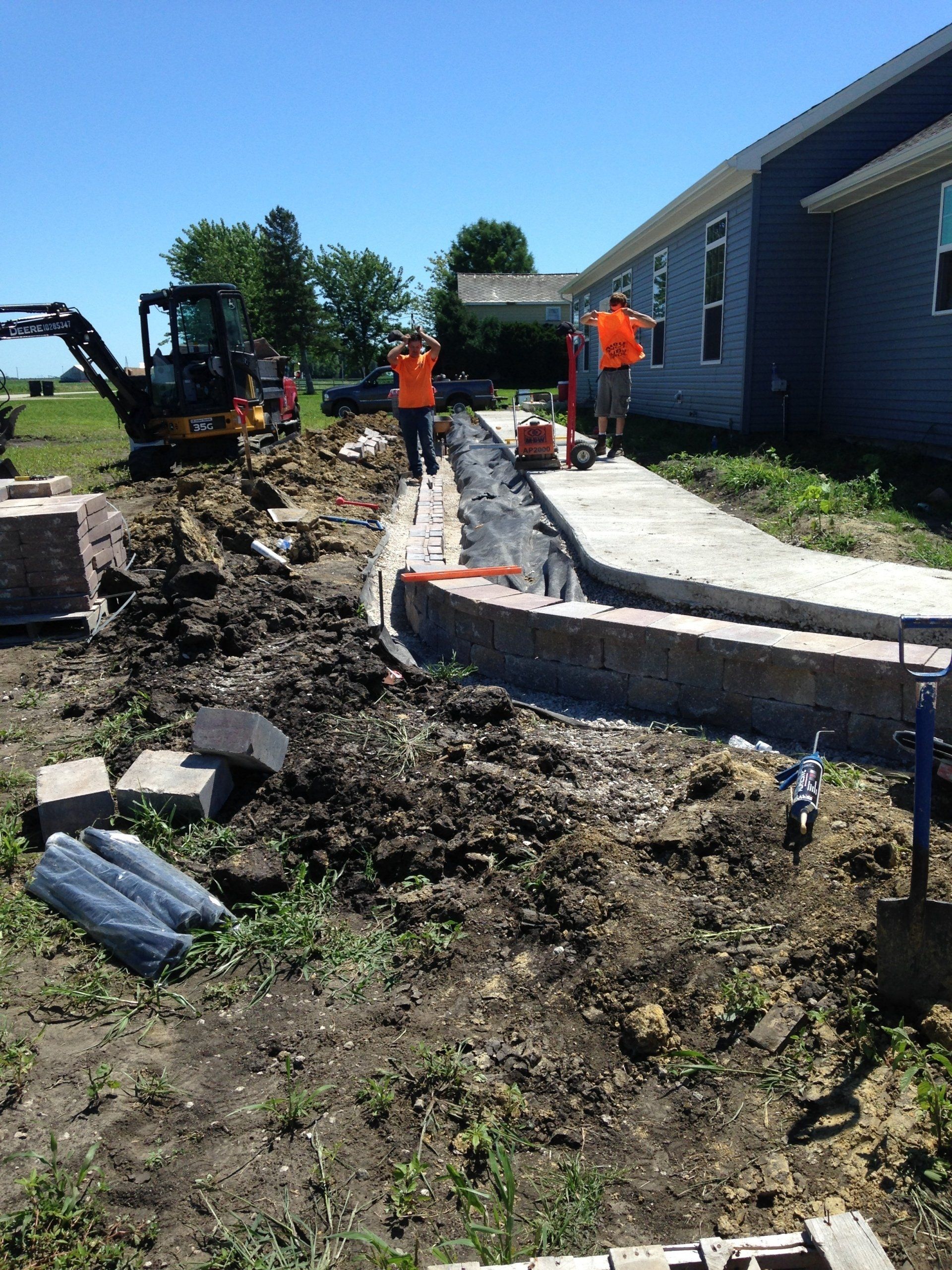 A group of construction workers are working on a sidewalk in front of a house.