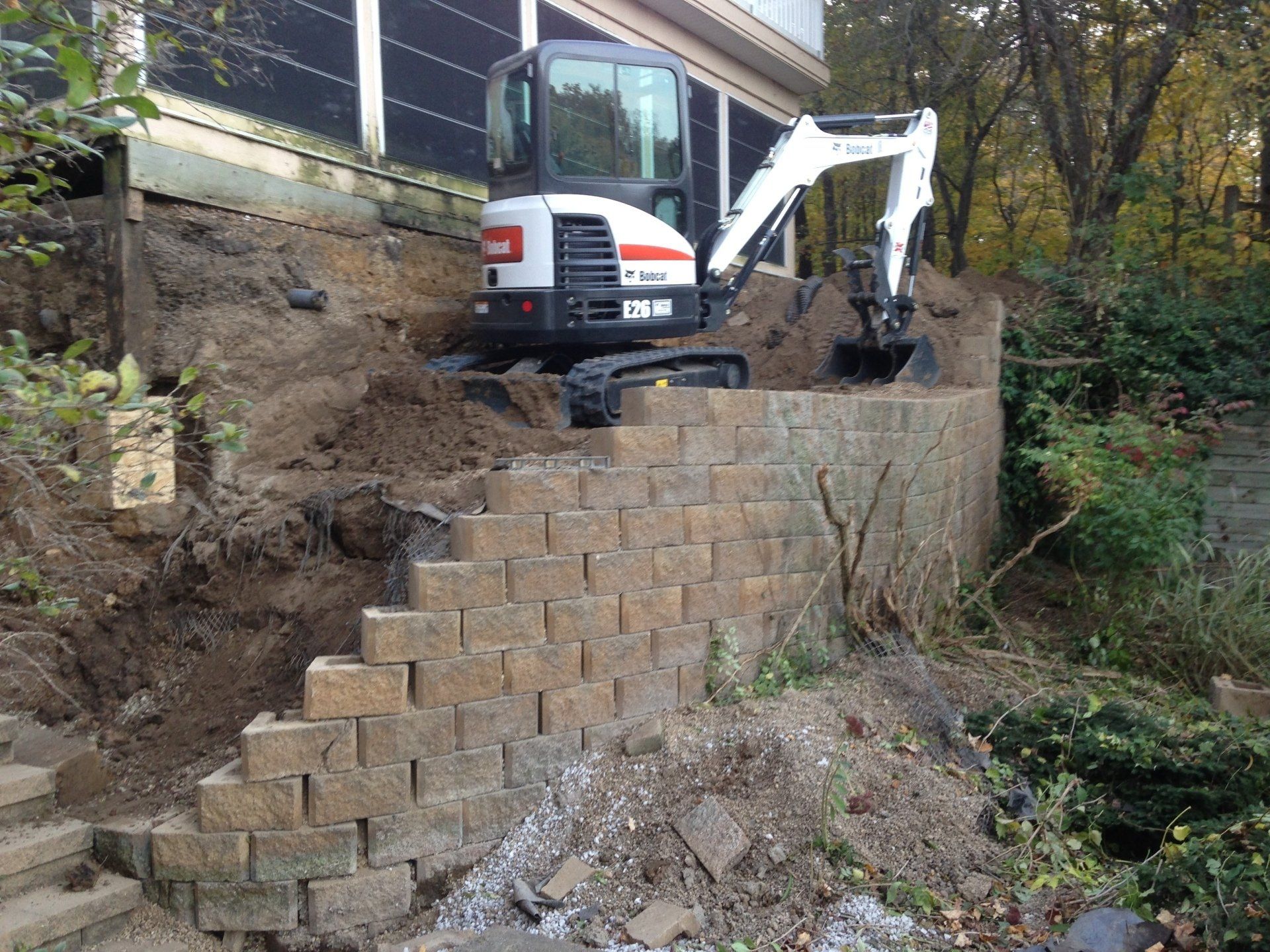 A bobcat excavator is working on a brick wall