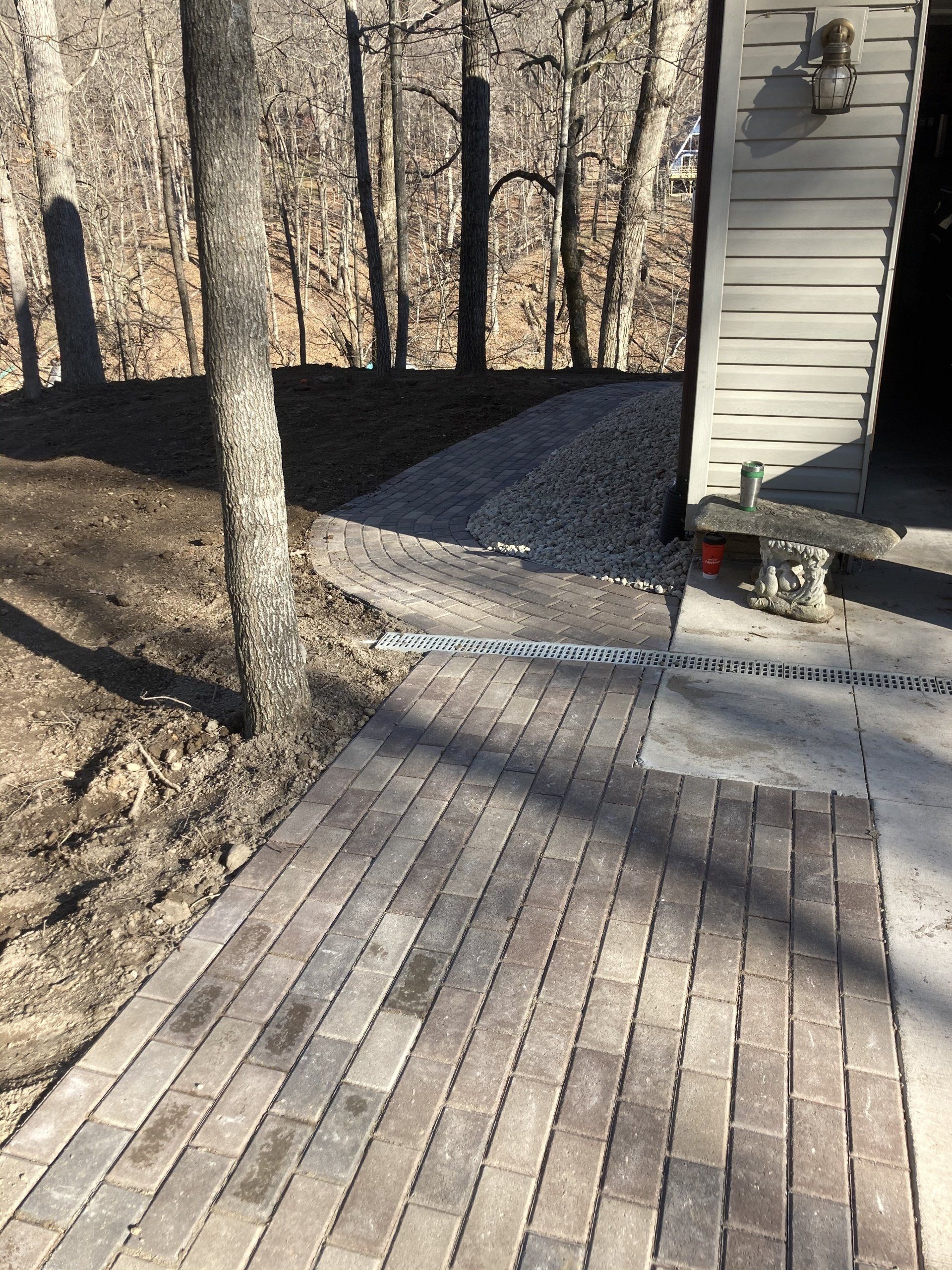 A brick walkway leading to a garage with trees in the background.