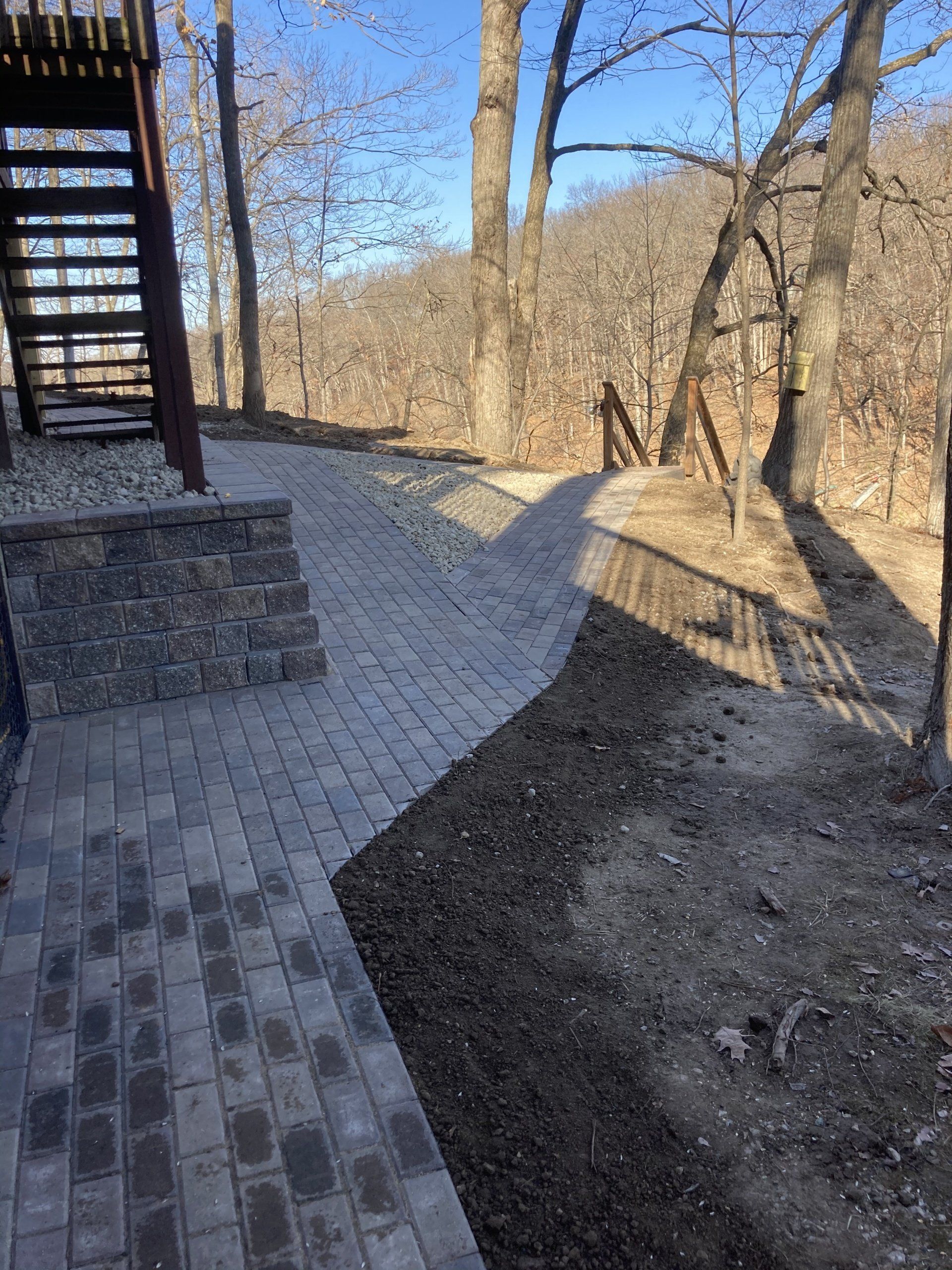 A brick walkway leading to a staircase in the woods.