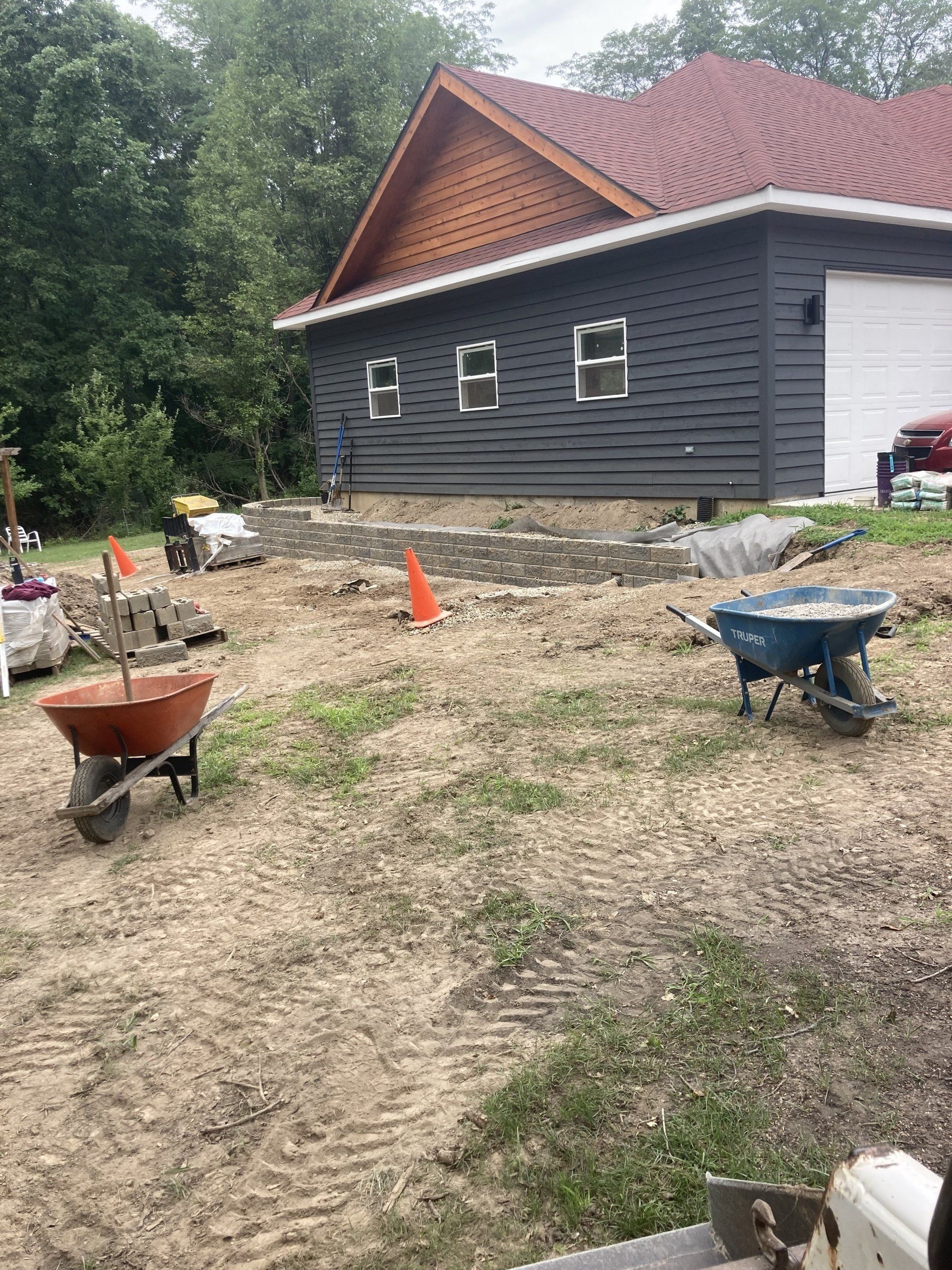 There are wheelbarrows in the dirt in front of a house.