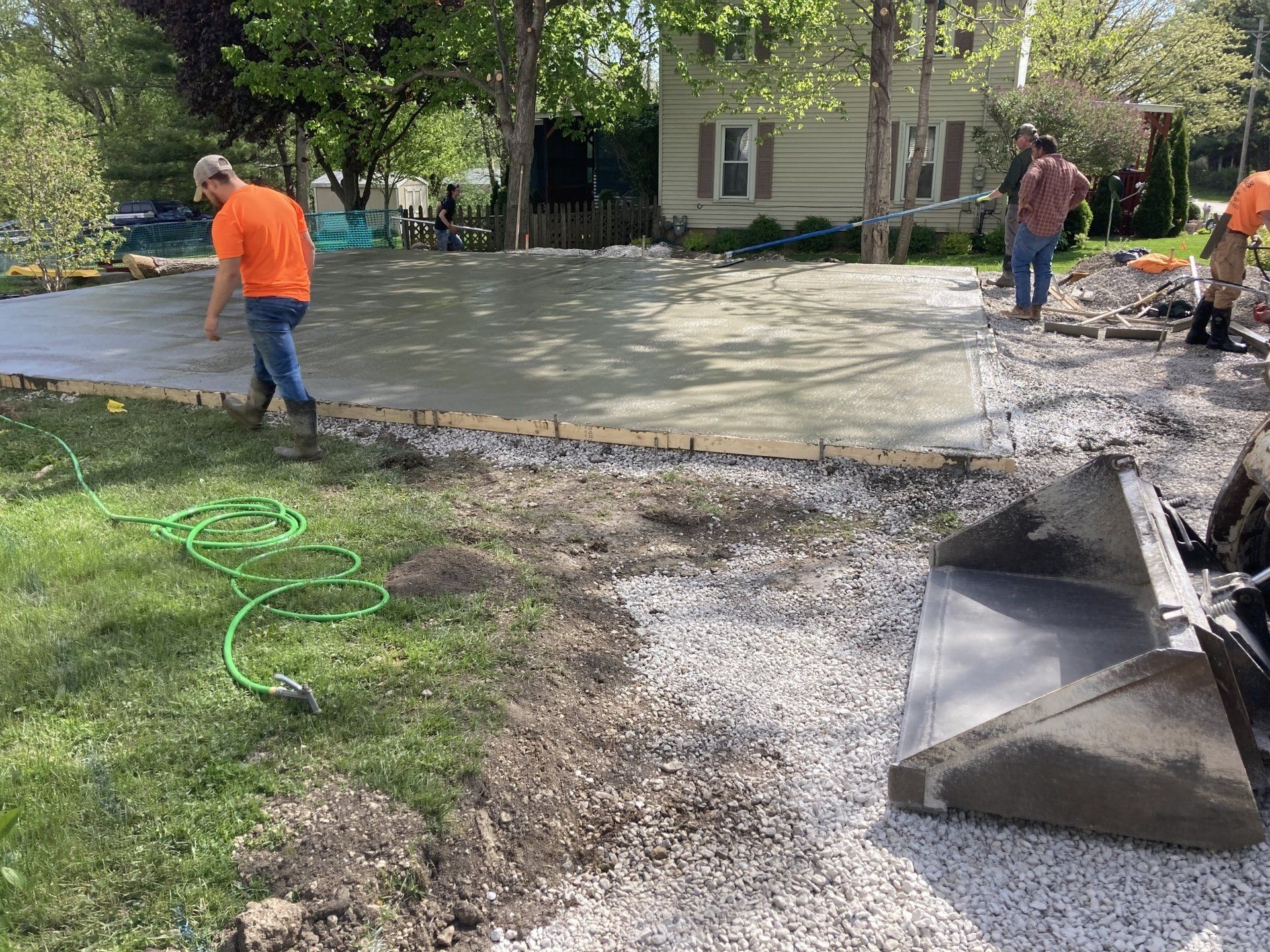 A group of men are working on a concrete driveway in front of a house.