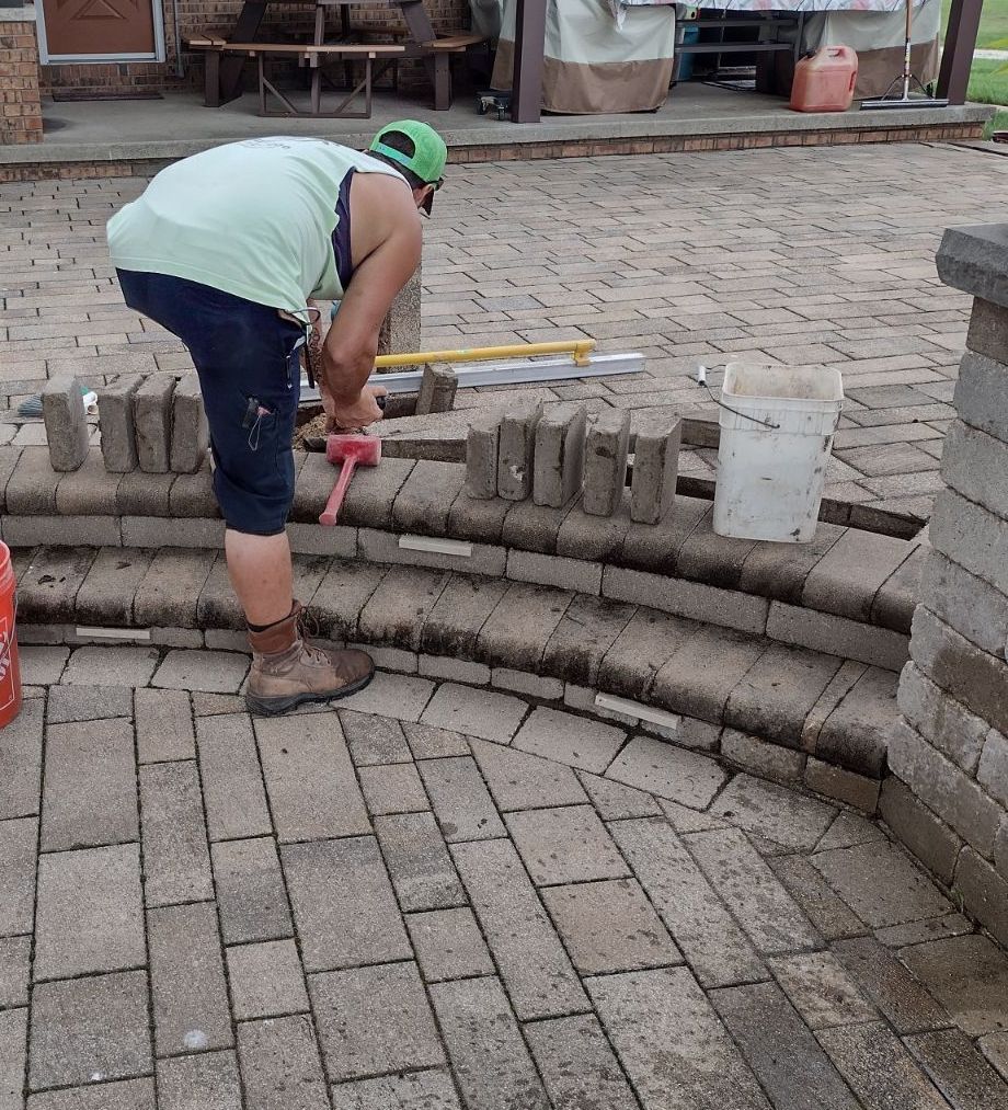A man is working on a brick walkway with a hammer