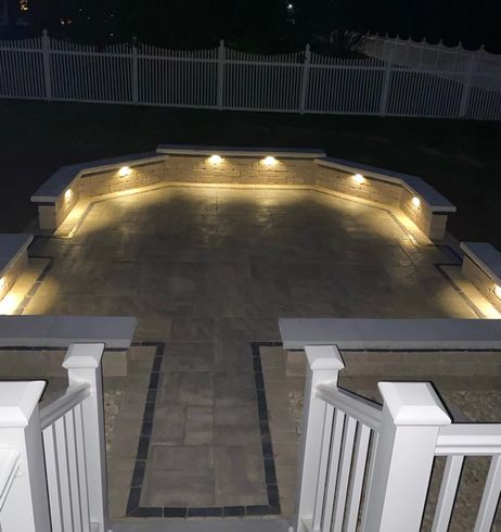 A patio is lit up at night with a white fence in the background