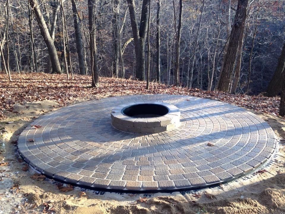 A fire pit is sitting on top of a brick patio in the middle of a forest.