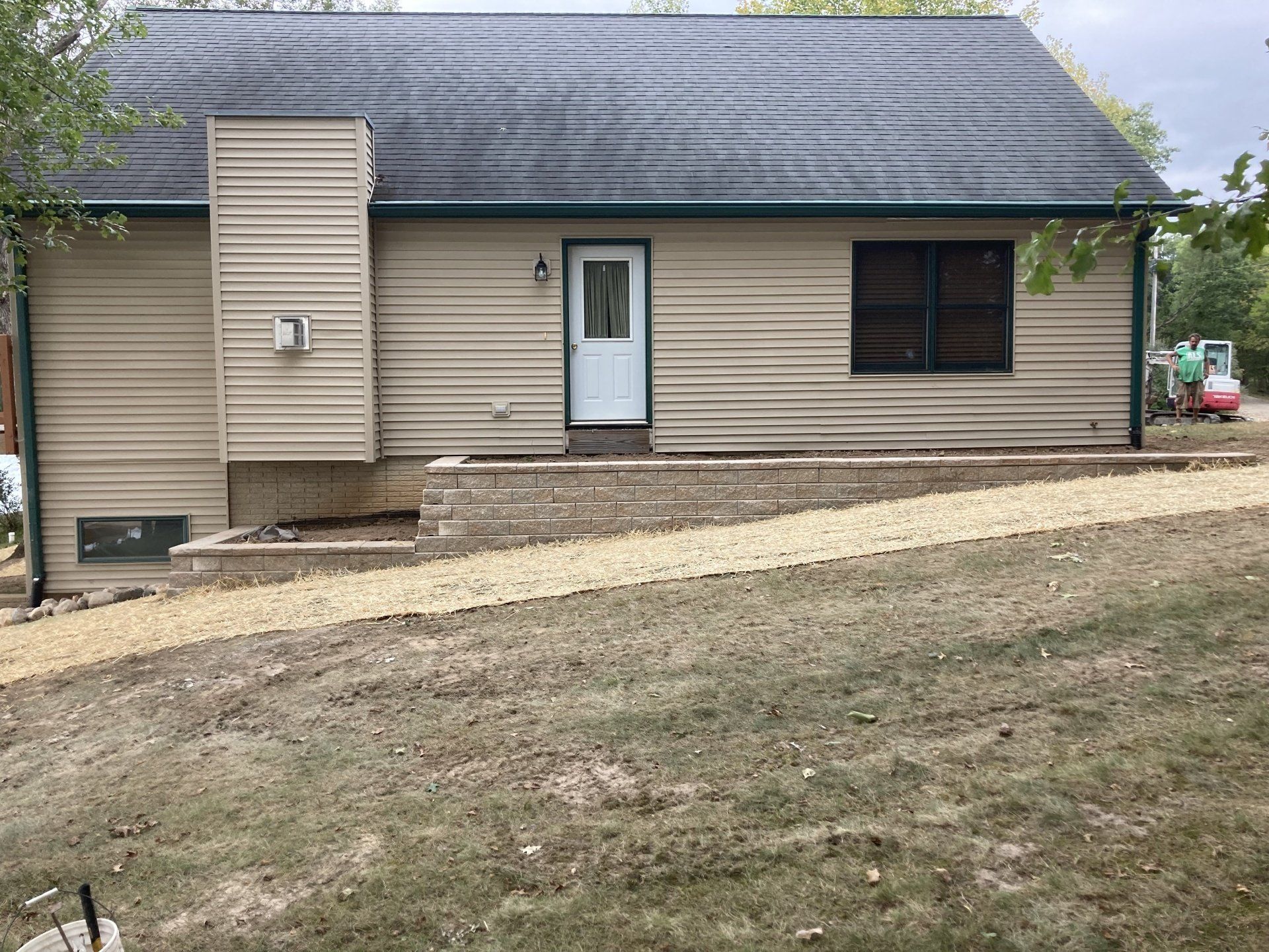 A small house with a blue door and a black roof is sitting on top of a grassy hill.