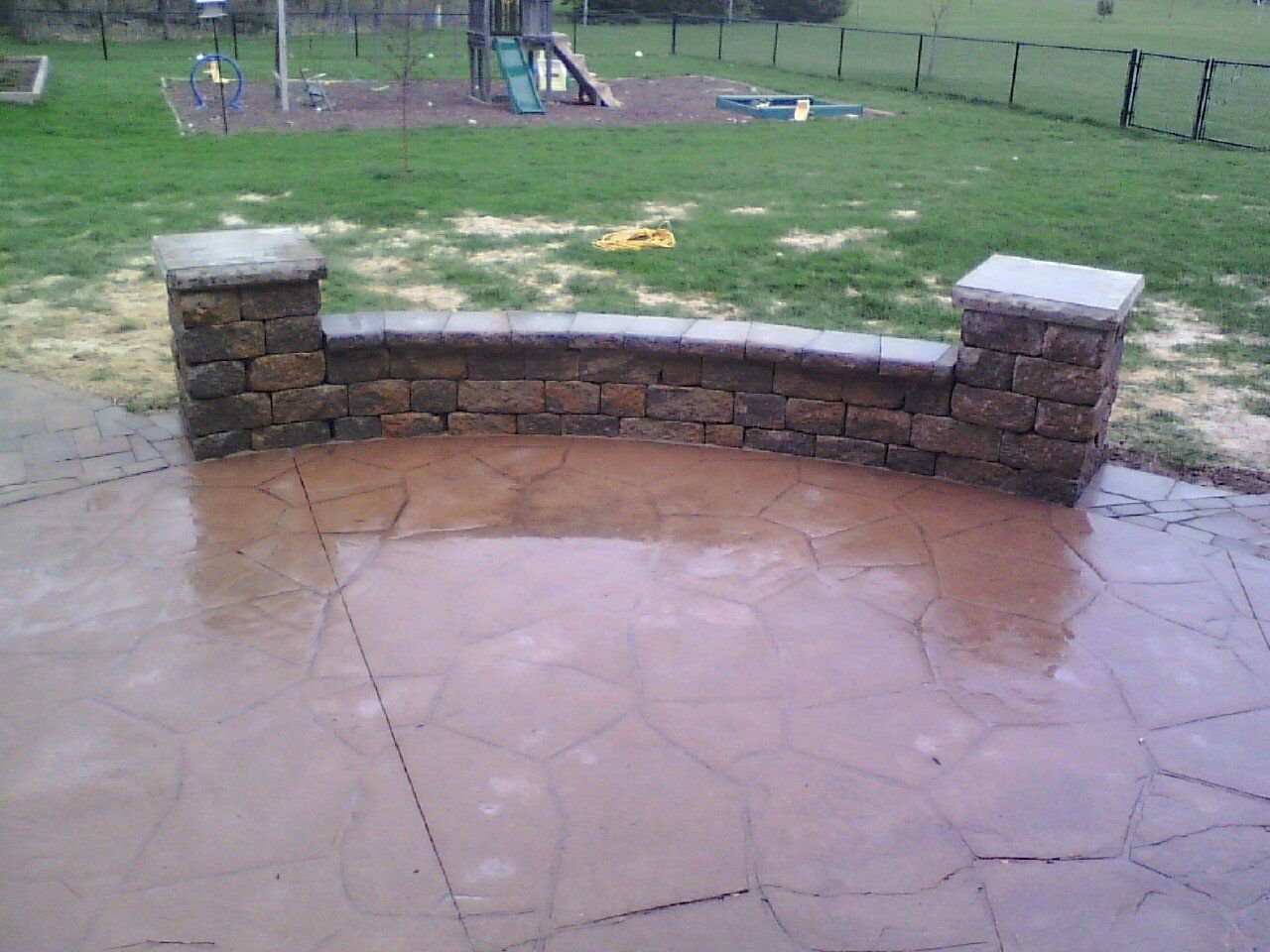 A patio with a stone wall and a playground in the background