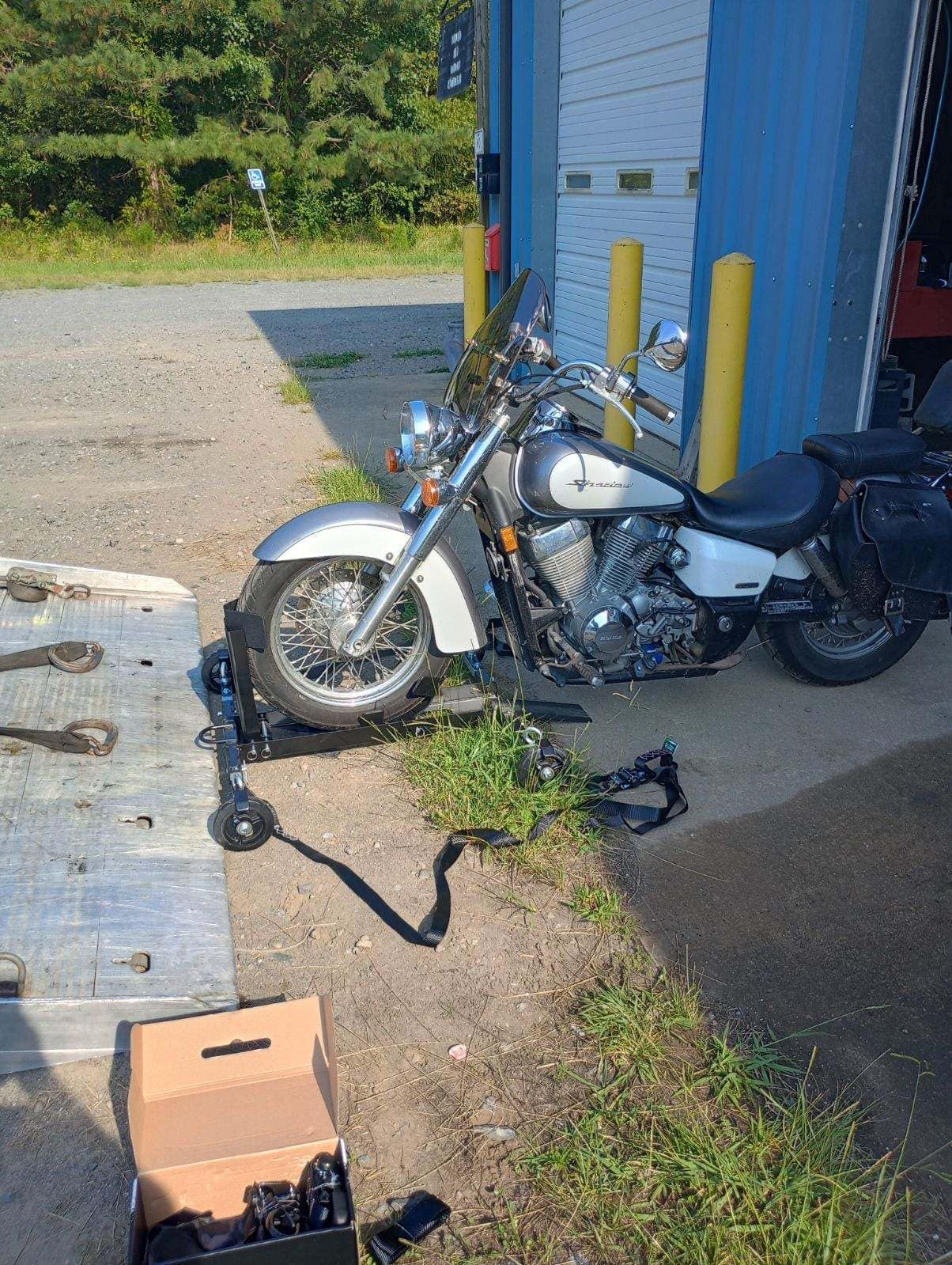 Silver and white motorcycle parked in front of a blue garage, on a lift, with a box of parts.